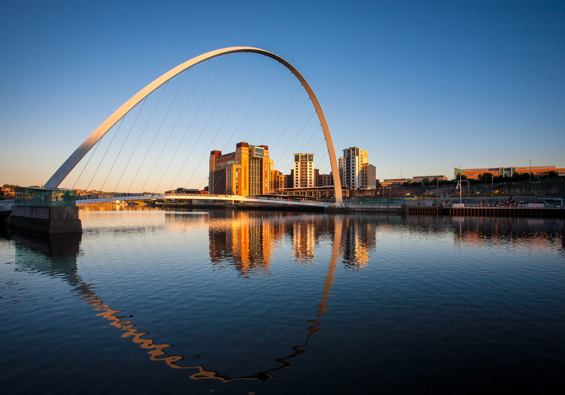 Millenium Bridge on Newcastle Quayside illuminated by the evening sun and reflected in the river Tyne